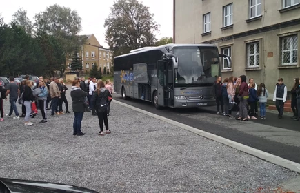 Na zdjęciu grupa os&oacute;b zbierająca się na parkingu na tle autobusu